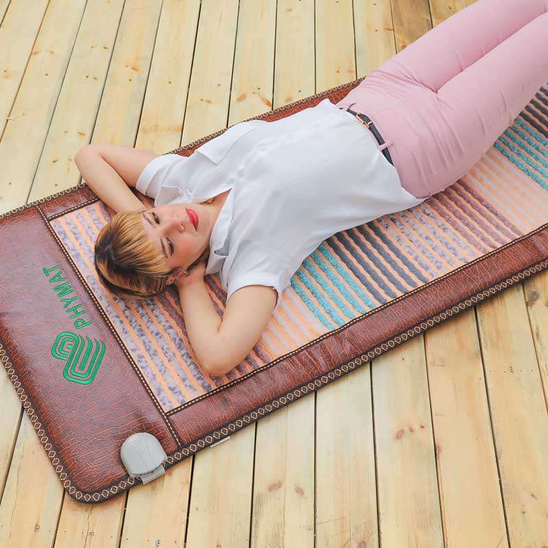 Woman relaxing on a PHYMAT gemstone infrared PEMF heating mat at home